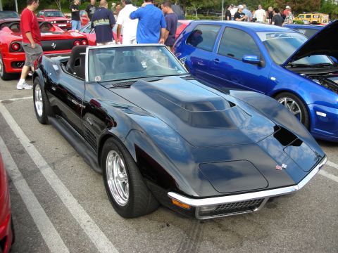 1998 Ford Crown Victoria - black Chevrolet Corvette convertible with chrome wheels and a custom hood parked among colorful cars and a crowd at a car show.