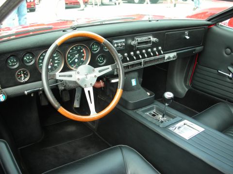 1998 Ford Crown Victoria - Black leather interior of a classic car showing a wood-rimmed steering wheel, round gauges, automatic shifter and a row of toggle switches.