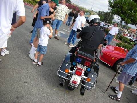 1998 Ford Crown Victoria - uniformed officer on a black touring police motorcycle moves through a crowd of people gathered in a parking lot at an event.