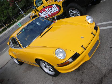 1998 Ford Crown Victoria - bright yellow vintage Porsche 911 coupe with round headlights parked on pavement next to a yellow Help-U-Sell branded truck.