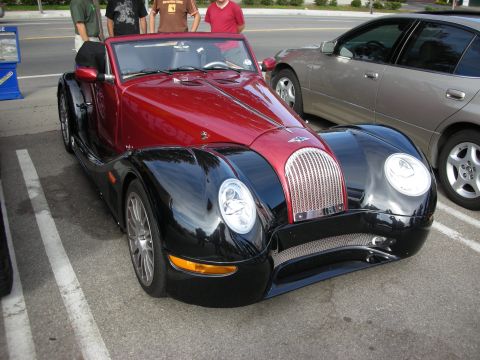 1998 Ford Crown Victoria - red-and-black retro-styled roadster with chrome mesh grille and round headlights parked among spectators at a car show.