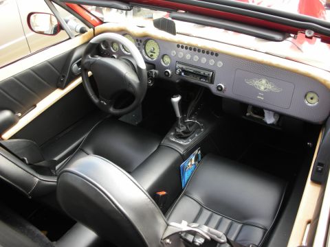 1998 Ford Crown Victoria - Black leather cockpit of an open roadster with a carbon-fiber dashboard, round gauges, manual shifter and a winged emblem on the dash.