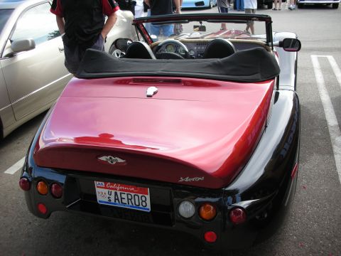 1998 Ford Crown Victoria - Rear view of a red-and-black open roadster with round taillights and a California license plate reading SAERO08 at a car show.