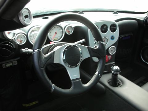 1998 Ford Crown Victoria - Cockpit of a sports car showing a silver-and-black three-spoke steering wheel, bank of white-faced gauges and a manual shifter.