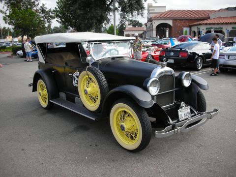 1998 Ford Crown Victoria - black vintage 1920s-era open touring car with a tan top and yellow wire-spoke wheels parked at an outdoor car show.