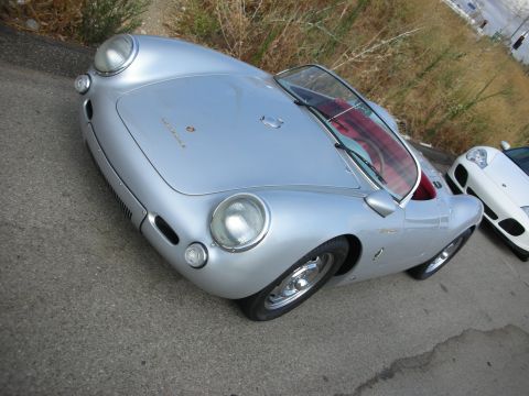 1998 Ford Crown Victoria - silver Porsche 550-style streamlined coupe with red interior and round headlights parked on pavement beside a white sports car.