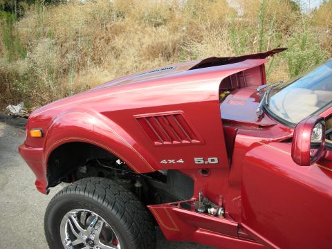 1998 Ford Crown Victoria - Front fender and open hood of a red coupe displaying 4X4 and 5.0 badges with louvered vents and a raised, lifted suspension.