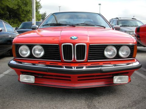 1998 Ford Crown Victoria - Front view of a red BMW 6-Series coupe with quad round headlights, kidney grille and BMW roundel parked in a lot.