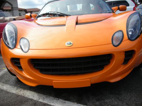 1998 Ford Crown Victoria - Close front view of an orange Lotus showing the oval Lotus badge, round headlights and gaping lower grille.