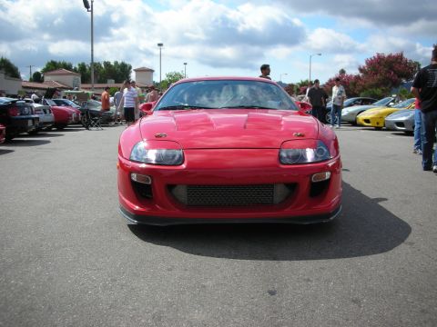 1998 Ford Crown Victoria - red Toyota Supra faces the camera showing a large front-mount intercooler and pop-up-style headlights at a car meet.