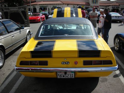 1998 Ford Crown Victoria - yellow Camaro SS with black racing stripes seen from behind, SS badge on the tail, parked among show cars.