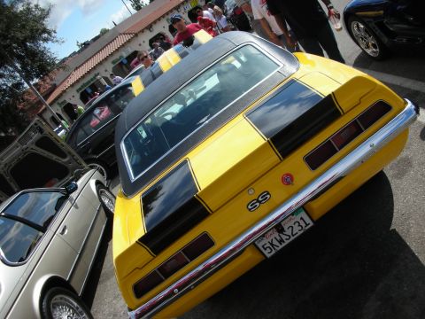 1998 Ford Crown Victoria - yellow Camaro SS with black stripes and a black roof, shot from a high rear three-quarter angle in a busy lot.