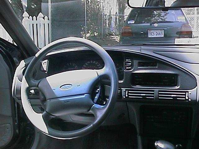 1993 Ford Taurus interior with a gray steering wheel and dashboard. A green Volkswagen is visible through the windshield