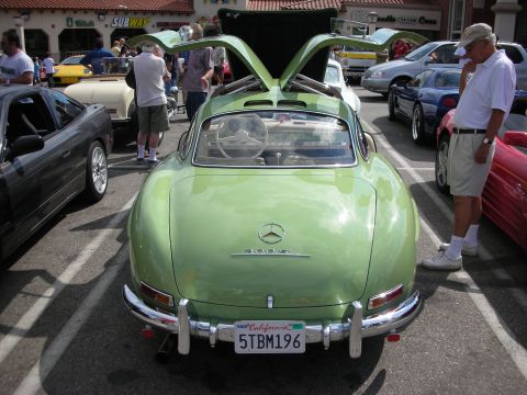 1998 Ford Crown Victoria - pale green Mercedes 300SL Gullwing coupe shown from the rear with both gullwing doors open at a car show.
