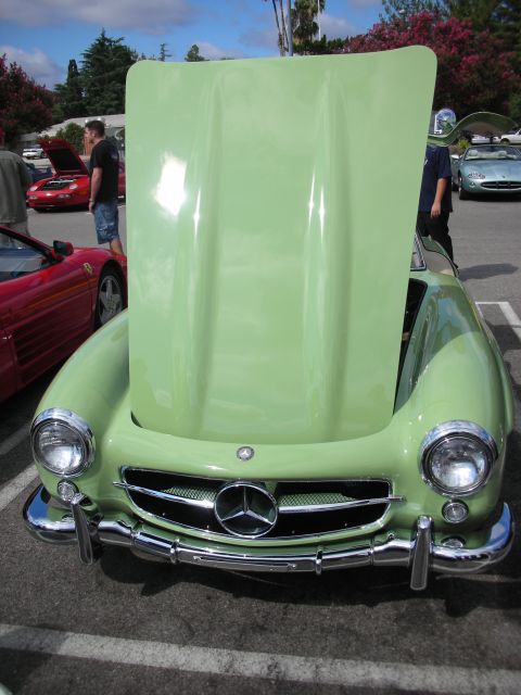 1998 Ford Crown Victoria - pale green Mercedes 300SL with its hood raised shows its star-and-bar grille; a red Ferrari sits alongside.
