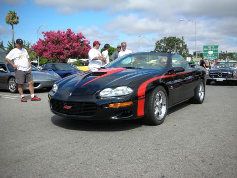 1998 Ford Crown Victoria - black Camaro convertible with a red side stripe and chrome wheels parked at a sunny car-show lot.
