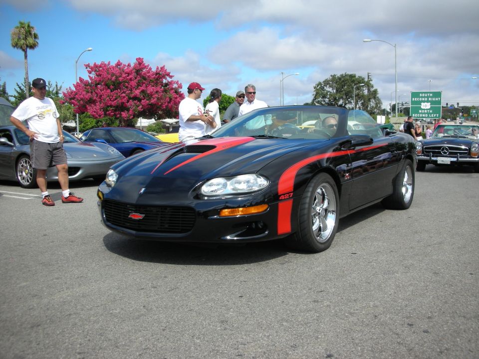 Front three-quarter of a black Camaro with red stripe at a meet