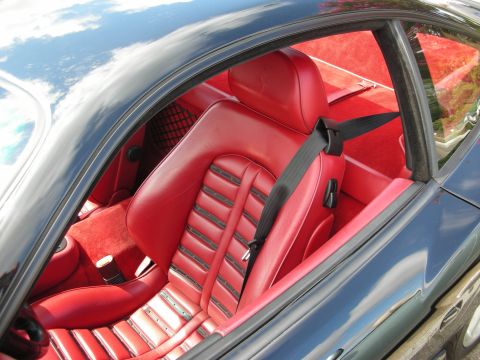 1998 Ford Crown Victoria - red leather driver's seat and black seatbelt of a coupe seen through the side glass, with sky reflecting in the dark paint.
