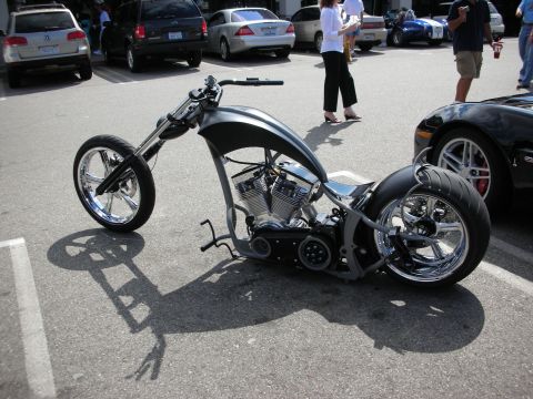 1998 Ford Crown Victoria - long silver custom chopper motorcycle with chrome spoke wheels and exposed V-twin engine parked on pavement at a show.