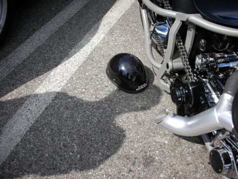 1998 Ford Crown Victoria - black half-shell motorcycle helmet resting on the asphalt next to a custom bike's chrome frame, drive chain and silver pipe.