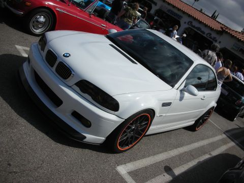 1998 Ford Crown Victoria - white BMW M3 coupe with a carbon-fiber hood, black mesh wheels and orange-lined rims parked at an outdoor show.