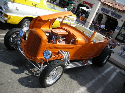 1998 Ford Crown Victoria - bright orange open-top hot rod roadster with a chromed engine, side exhaust pipes and chrome wheels parked on a street.