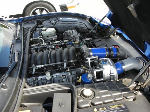 1998 Ford Crown Victoria - Close-up of a Corvette V8 engine bay showing the intake manifold, brake reservoir and blue intercooler piping of a supercharger.