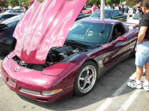 1998 Ford Crown Victoria - maroon Chevrolet Corvette with the hood raised and polished five-spoke wheels, surrounded by spectators at a car show.