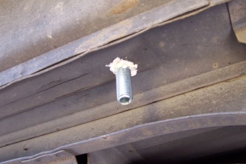 1990 Ford Bronco - A close-up view of a bolt protruding from the rusty undercarriage of a vehicle.