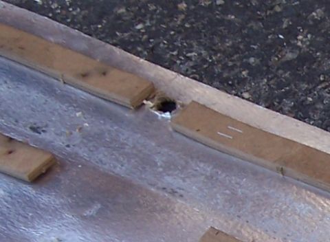 1990 Ford Bronco - A close-up view of a metal surface with wooden planks and a hole, possibly part of a vehicle's undercarriage or a trailer.