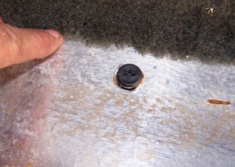 1990 Ford Bronco - Close-up of a screw securing a carpeted surface, with a finger indicating the area.