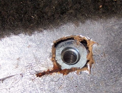 1990 Ford Bronco - A close-up view of a threaded metal anchor point, showing wood shavings and signs of rust.