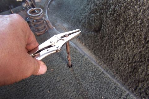 1990 Ford Bronco - Vise grips are used to remove a rusty bolt from a carpeted area, possibly inside a vehicle.