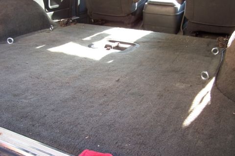 1990 Ford Bronco - The carpeted cargo area of a vehicle shows several tie-down rings and the rear seats.