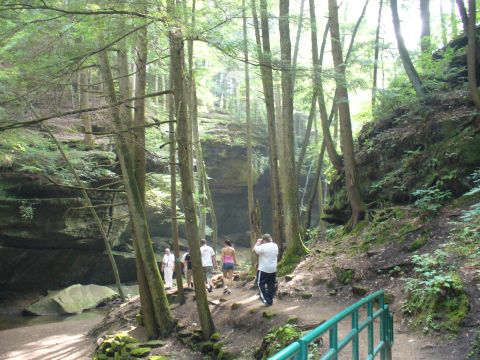 1991 Ford Probe - A group of people explore a scenic forest trail leading to a cave entrance.