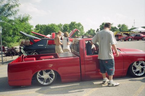 1995 Ford Probe - A red pickup truck is parked at a car show with its hood up, alongside other vehicles.