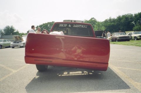 1995 Ford Probe - Rear view of a red pickup truck at an outdoor event with other cars present.