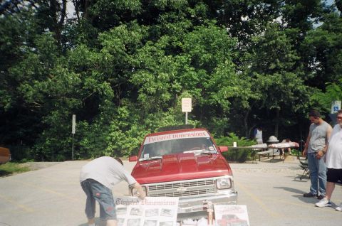 1995 Ford Probe - A red pickup truck is displayed at an outdoor event with a person examining display boards in front of it.