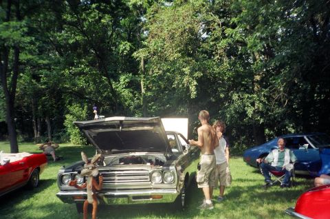 1995 Ford Probe - A car show features several vehicles and people gathered around a black car with its hood up.