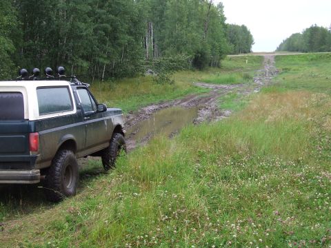 1988 Ford Bronco - A Ford Bronco navigates a muddy track through a wooded area.