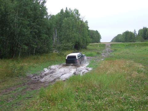 1988 Ford Bronco - A 1988 Ford Bronco navigates a muddy trail surrounded by trees.