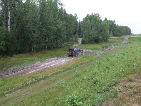 1988 Ford Bronco - A dark-colored SUV navigates a wet, muddy path surrounded by dense green trees and vegetation.