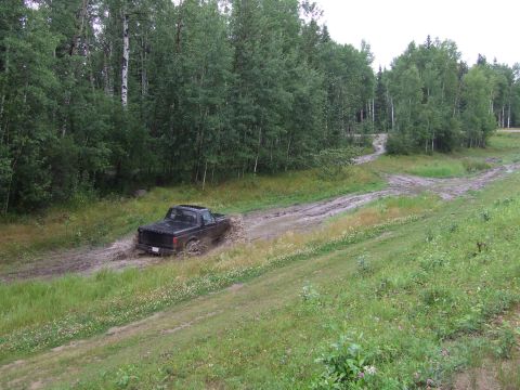 1988 Ford Bronco - A black pickup truck navigates a muddy trail surrounded by trees. The vehicle is identified as a 1988 Ford Bronco.