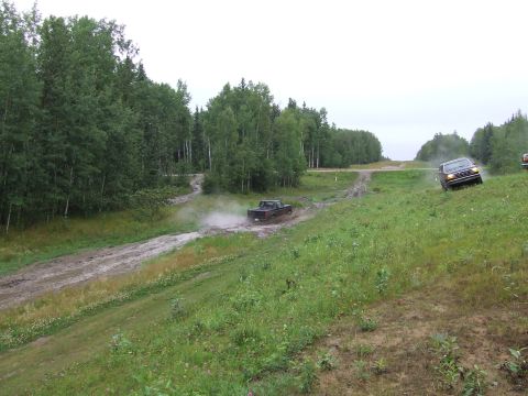 1988 Ford Bronco - Two vehicles navigate challenging off-road terrain with muddy tracks and grassy inclines under an overcast sky.
