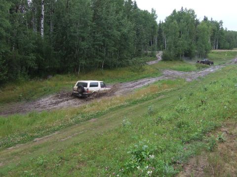1988 Ford Bronco - A white 1988 Ford Bronco navigates a muddy trail, with another vehicle visible in the distance.