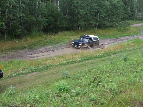 1988 Ford Bronco - A black Ford Bronco navigates a muddy trail, kicking up water.
