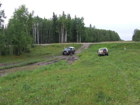 1988 Ford Bronco - Two SUVs navigate a challenging off-road course with muddy terrain and grassy slopes.