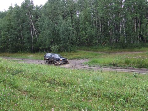 1988 Ford Bronco - A dark SUV navigates a muddy track through a wooded area.