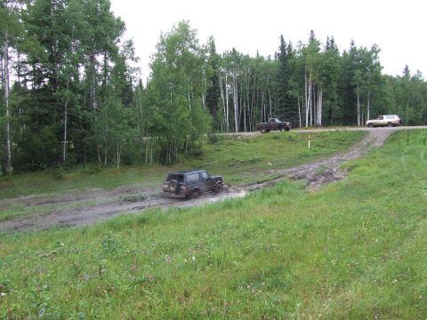 1988 Ford Bronco - Multiple vehicles traverse a muddy trail surrounded by trees.