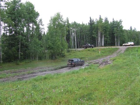1988 Ford Bronco - Several off-road vehicles navigate a wet and muddy trail surrounded by a dense forest.